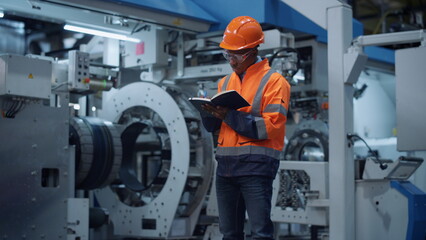 Male engineer taking notes of project data at manufacturing factory.