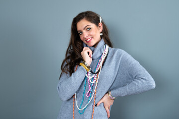 elegant woman in a long gray sweater has fun with many bead chains and jewelry, isolated on gray