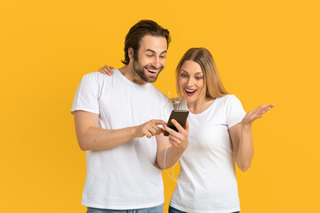 Cheerful millennial european husband in white t-shirt show phone to surprised wife