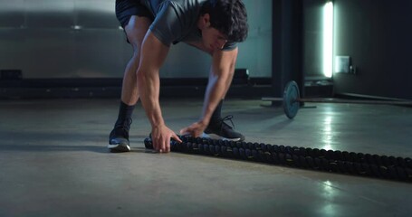 Cinematic shot of young fit virtual instructor or online personal trainer is showing web training workouts with battle ropes in sports studio gym.