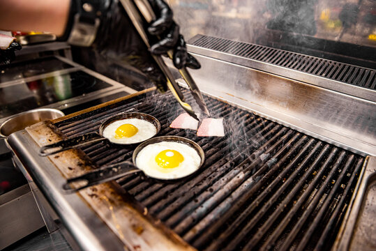 chef cooking Eggs and bacon in pan on grill in kitchen