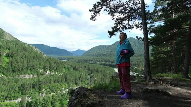 Active Elderly woman with yoga mat walking on top of a mountain after exercise, enjoying nature and scenery landscape outdoor