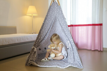 Cute toddler girl sitting in wigwam with her teddy bear in bedroom  © triocean
