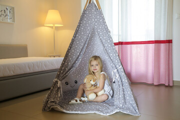 Cute toddler girl sitting in wigwam with her teddy bear in bedroom  © triocean