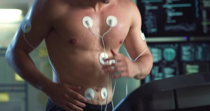 Cinematic close up shot of young athlete with medical electrodes doing endurance test of body resistance by training on treadmill with monitoring heart rate, pulse and ECG data in modern laboratory.