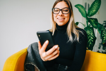 Young cheerful attractive woman in eyeglasses using mobile phone at home.