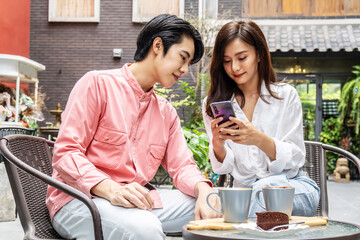 Happy Young asian woman sitting with boyfriend at cafe table, discussing over on smartphone, Young couple looking at mobile phone shopping online and share information together in coffee shop