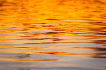 Defocused abstract background of bright orange and blue waves on river during sunset 