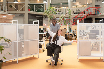 multi-ethnic business colleagues having fun in the work break sitting in the office wheelchair in a coworking space