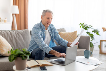 Man holding paper reading report working on laptop at home