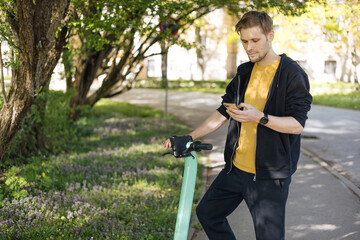 Transportation ecology. Green sustainable mobility Young man unlocks an e-scooter with his mobile phone. Electric scooter new way city. Green transportation. Sustainable climate neutral cities goals.