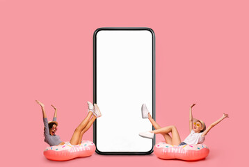 Cheerful Young Women Sitting In Inflatable Pool Rings Next To Blank Smartphone