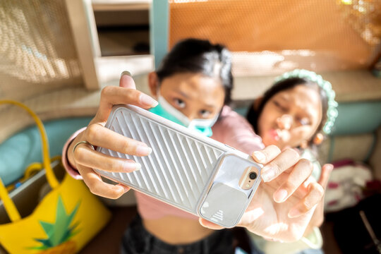 Asian teenage girl wear face mask doing selfie together with sister using smartphone in a restaurant