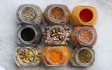 Close up photo of various spices in glass jars. Cardamom, flax seeds, mixed pepper, lavender, curry and turmeric. 