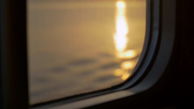 lateral image from the window of a cruise ship where the camera goes up and shows us a wonderful sunset on a summer day with the sun is yellow and orange during a change of focus  show us the sea