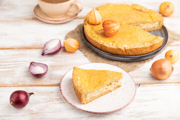 Autumn onion pie and cup of coffee on white wooden background. Side view, selective focus.