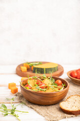 Fototapeta na wymiar Vegetarian vegetable salad of tomatoes, pumpkin, microgreen pea sprouts on white wooden background. Side view, copy space.