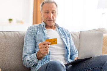Smiling mature man using pc and credit card at home