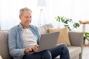 Confident casual mature using pc sitting on sofa