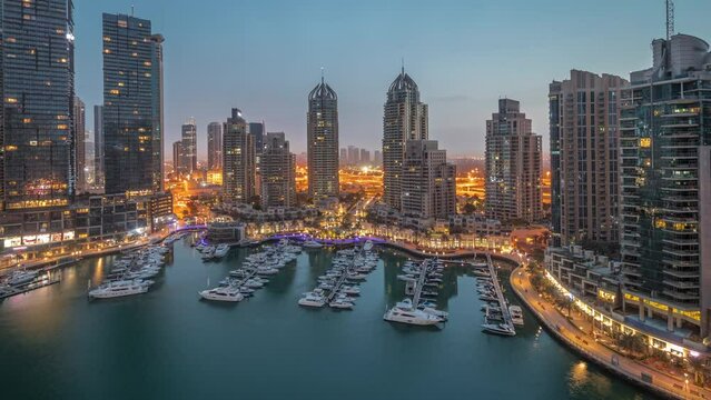 Luxury yacht bay in the city aerial night to day transition timelapse in Dubai marina panorama before sunrise. Modern skyscrapers along waterfront promenade and boats floating in harbor