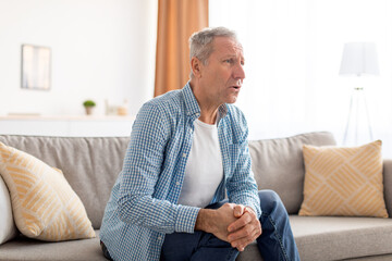 Mature man with knee pain sitting on couch at home