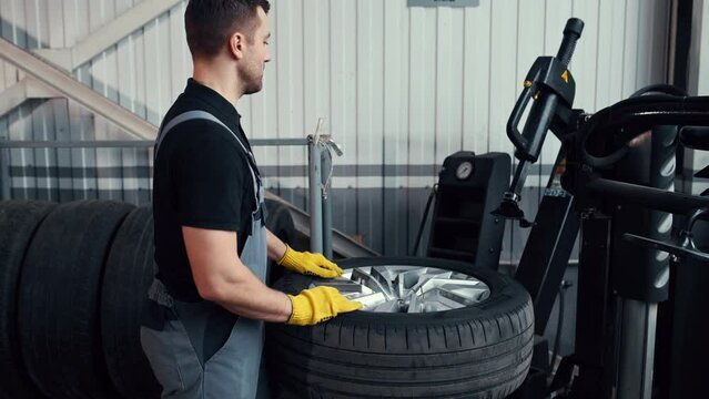 Putting wheel into fixation device. Man in uniform is in the automobile repair shop