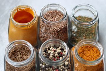 Close up photo of various spices in glass jars. Cardamom, flax seeds, mixed pepper, lavender, curry...