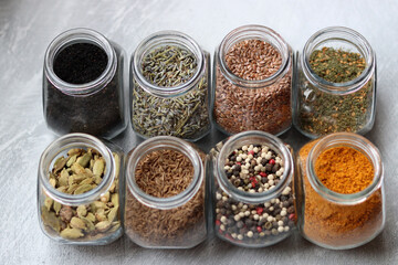 Different types of spices in glass jars. Close up photo of food flavors. Cardamom, turmeric, lavender, curry, pepper and flax seeds. 