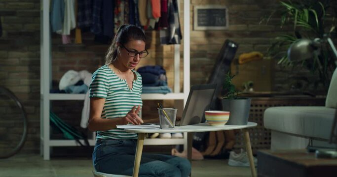 Cinematic shot of young woman is making video conference call to colleagues or partners with laptop while doing smart working from home during lockdown.