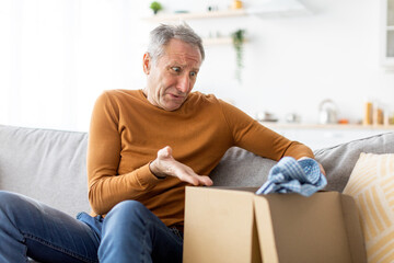 Sad mature man unpacking wrong parcel, delivery mistake
