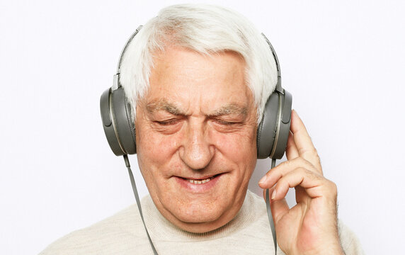 Lifestyle, tehnology and old people concept: image of an elderly gray-haired man listening to music with headphones