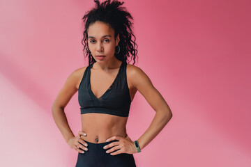 attractive black african american woman in black leggins fitness outfit on pink background