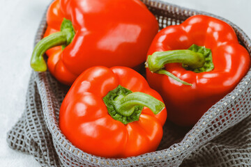 Fresh ripe sweet red bell peppers in eco-friendly reusable produce bag on gray background. Healthy grocery, vegan food and ingredients for cooking concept. Close-up
