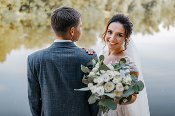The wedding couple smiles and pauses for the camera. A river in the background. The bride has a...