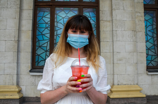 Young woman wearing face surgical mask is thinking how to drink a cocktail. Quarantine. New reality. Quarantine misunderstanding