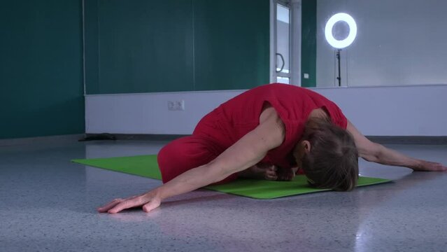 Elderly woman doing yoga exercise in studio alone, bending over with bent legs in butterfly pose