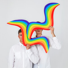 two young men hold pieces of the rainbow and hide their faces behind the decor, concept of LGBTQ...
