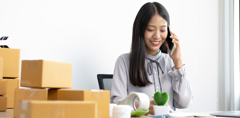 Asian businesswoman is taking online orders from a phone and chatting with customers to confirm their order, Selling products online or doing freelance work at home concept.