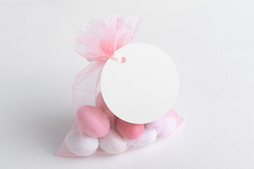 Round white tag mockup with gift with pink chocolate confetti in a bag with pink ribbon. Wedding favor tag for souvenir o gift for gues, sign for message greeting, close up, element for design