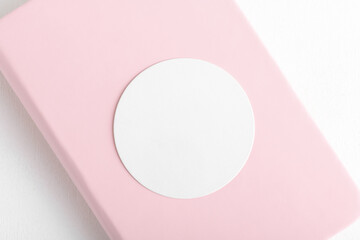 Round sticker mockup, circle white adhesive label mockup in pink book on a white background, close...