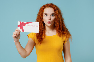 Young amazed happy redhead woman 20s wear yellow t-shirt hold gift certificate coupon voucher card...