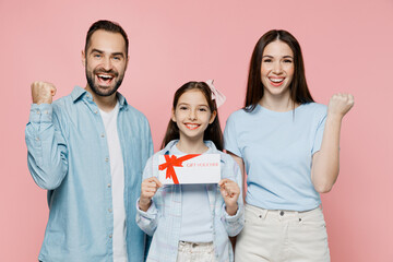 Young happy fun parents mom dad with child kid daughter teen girl in blue clothes hold gift certificate coupon voucher card for store do winner gesture isolated on plain pastel light pink background