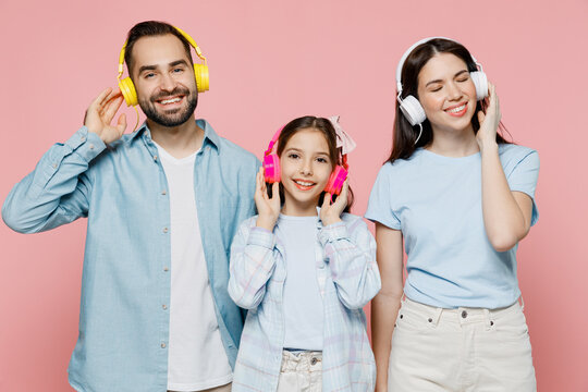 Young happy smiling cheerful parents mom dad with child kid daughter teen girl in blue clothes headphones listen to music have fun isolated on plain pastel light pink background. Family day concept.
