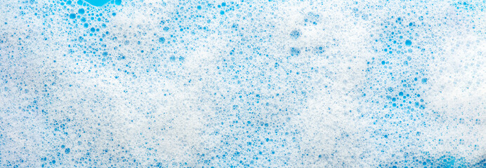 Texture of white foam on a blue background. Cleansing mousse for the face or shaving foam or washing powder. Closeup