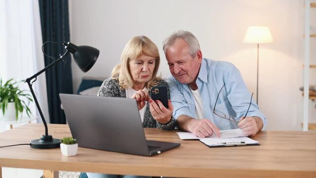 Using smartphone. Scrolling the device. Couple of cute old people that is indoors at home