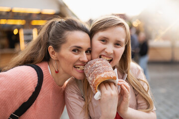 smiling mother and daughter at fair in city eating trdelnik