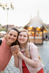 smiling mother and daughter at fair in city eating trdelnik