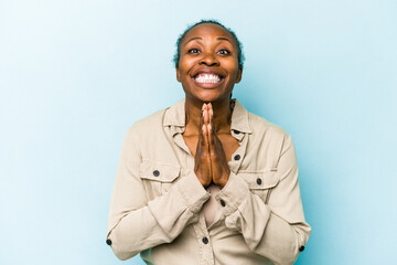 Young african american woman isolated on blue background holding hands in pray near mouth, feels confident.