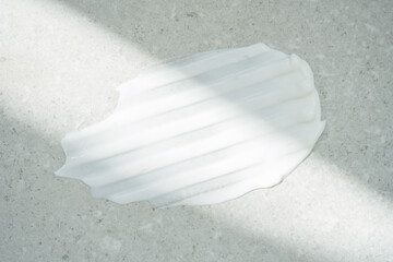 Sample of cream smear under sunlight. White cream or body lotion texture on gray concrete stone...