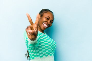 Young african american woman isolated on blue background joyful and carefree showing a peace symbol with fingers.